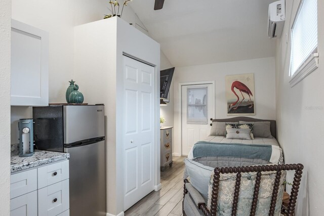 bedroom featuring a wall unit AC, wood tiled floor, freestanding refrigerator, vaulted ceiling, and multiple windows