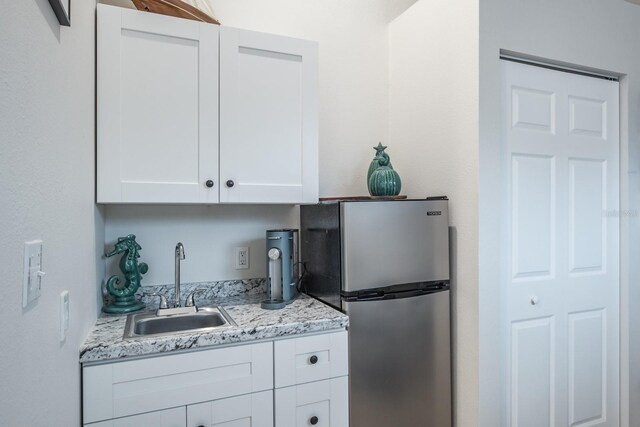 kitchen featuring white cabinets, light stone countertops, freestanding refrigerator, and a sink