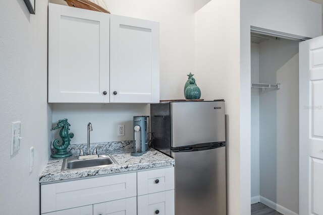 kitchen with a sink, light stone counters, white cabinetry, freestanding refrigerator, and baseboards