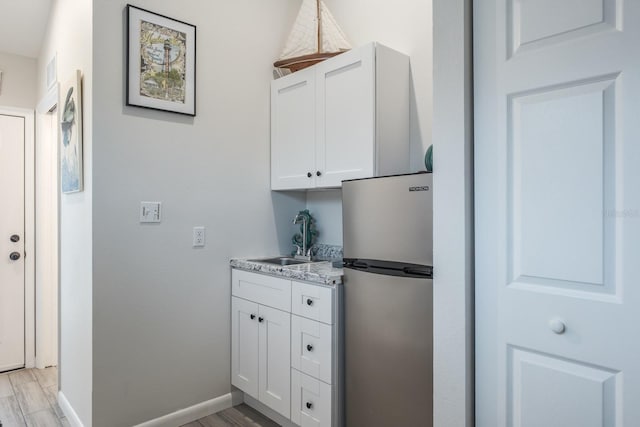 kitchen with a sink, light wood finished floors, white cabinetry, and freestanding refrigerator