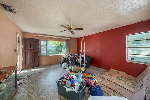 living area with a textured ceiling, a textured wall, visible vents, and ceiling fan