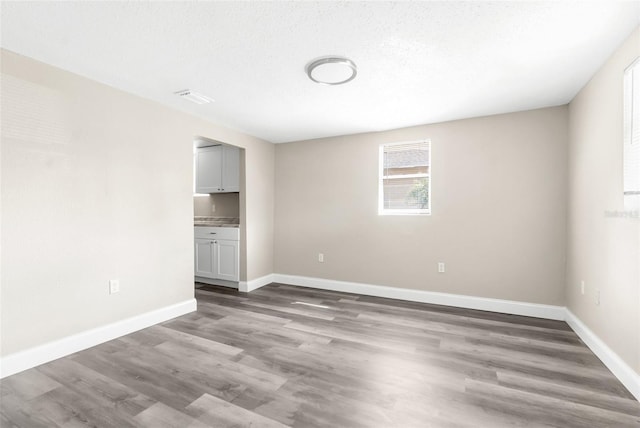 unfurnished room with visible vents, a textured ceiling, baseboards, and wood finished floors