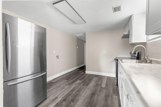 kitchen featuring visible vents, dark wood-type flooring, freestanding refrigerator, white cabinets, and a sink