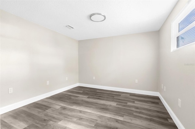 empty room featuring visible vents, a textured ceiling, baseboards, and dark wood-style flooring