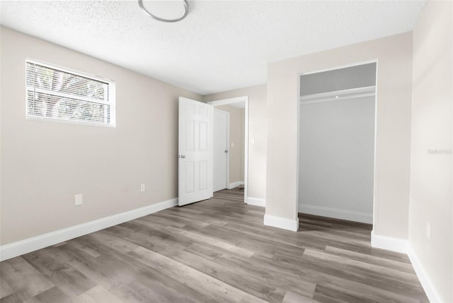 unfurnished bedroom with a textured ceiling, baseboards, and wood finished floors