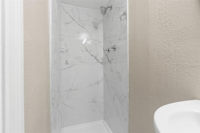 bathroom featuring a marble finish shower and a textured wall