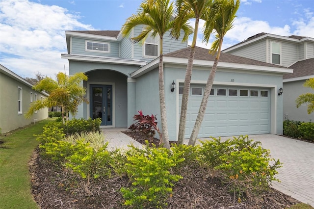 view of front of home featuring roof with shingles, an attached garage, driveway, and stucco siding