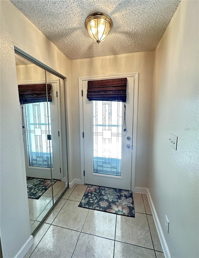 doorway to outside featuring a textured wall, baseboards, a textured ceiling, and tile patterned flooring