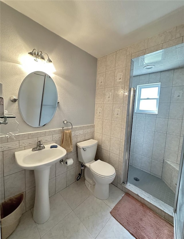 full bathroom with tile patterned floors, a wainscoted wall, toilet, tile walls, and a shower stall