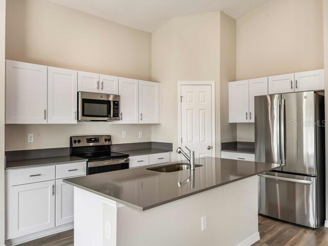 kitchen featuring dark countertops, a high ceiling, white cabinets, stainless steel appliances, and a sink