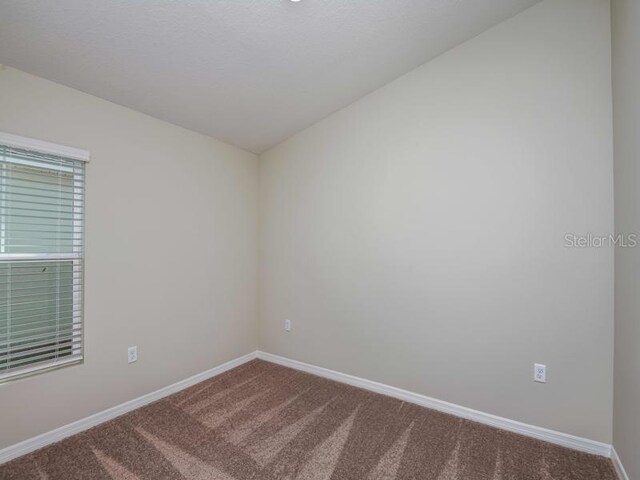 carpeted spare room featuring lofted ceiling and baseboards