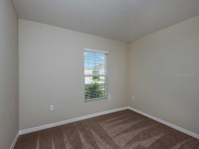 empty room featuring dark colored carpet, baseboards, and a textured ceiling