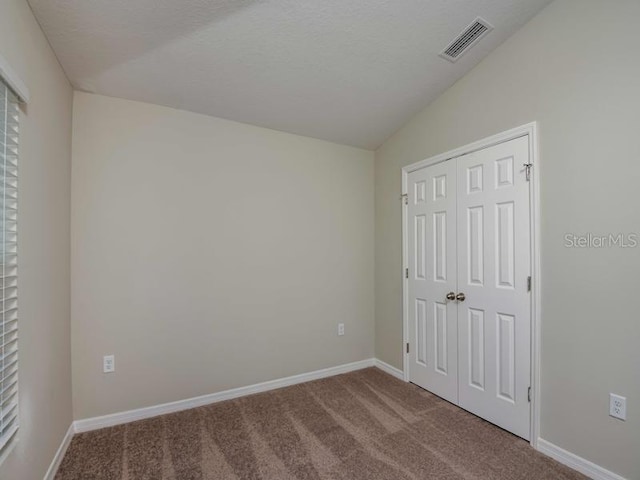 unfurnished bedroom with visible vents, baseboards, lofted ceiling, carpet floors, and a textured ceiling