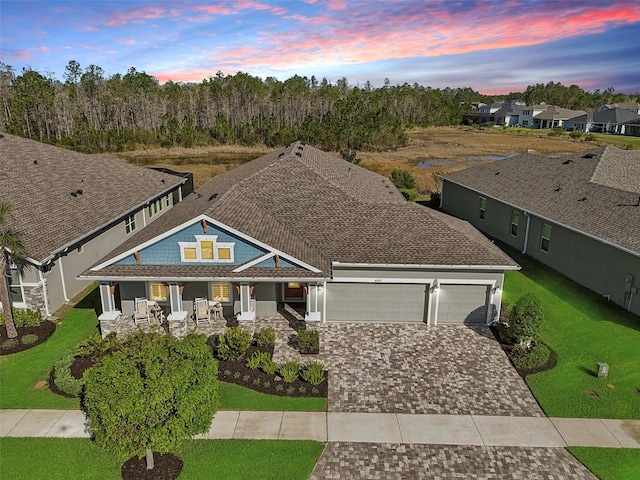 view of front of home featuring decorative driveway, covered porch, a front yard, a shingled roof, and a garage