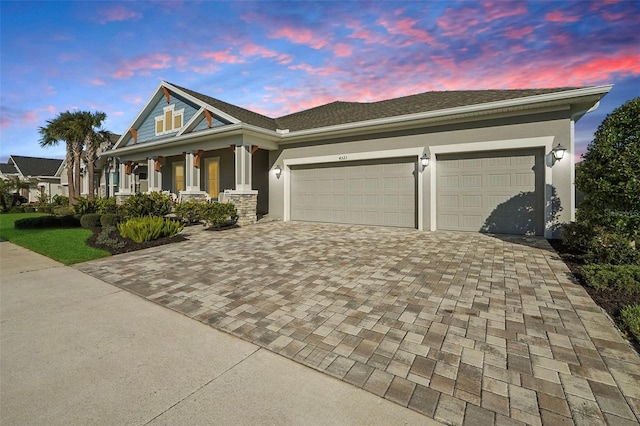 view of front of house with covered porch, stucco siding, decorative driveway, and a garage