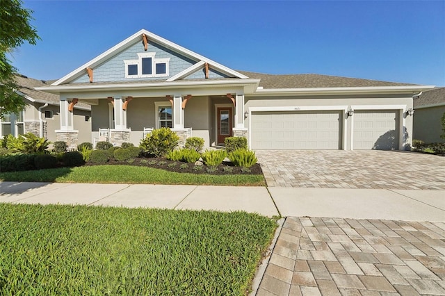 craftsman house featuring covered porch, stucco siding, driveway, and an attached garage