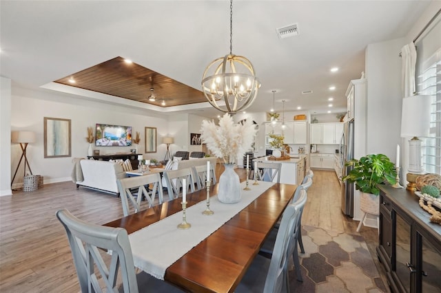 dining area with a tray ceiling, a notable chandelier, visible vents, and light wood-style flooring