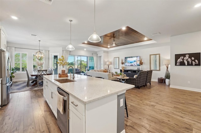 kitchen featuring visible vents, light wood-type flooring, stainless steel appliances, a raised ceiling, and a sink