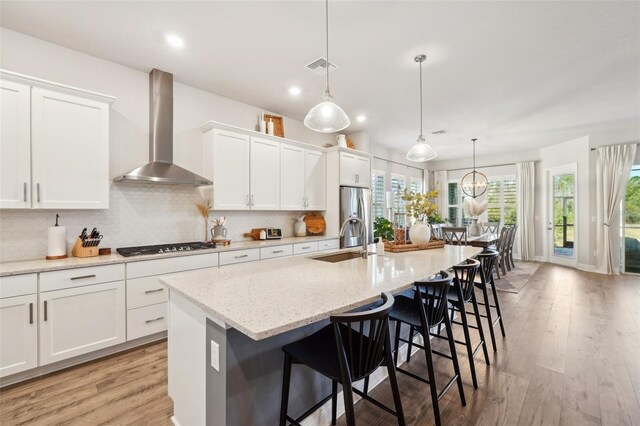 kitchen with an island with sink, a sink, backsplash, freestanding refrigerator, and wall chimney exhaust hood