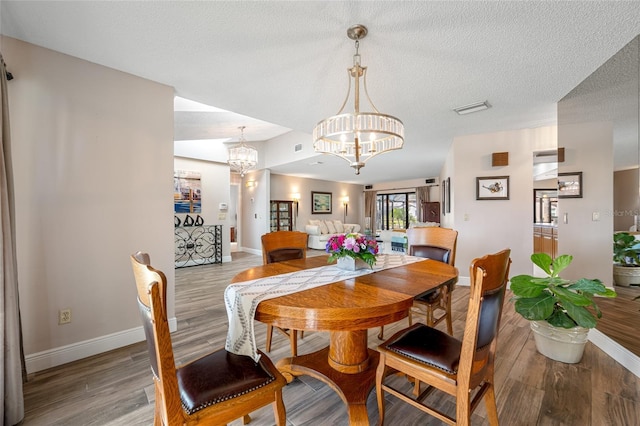 dining area with visible vents, baseboards, wood finished floors, a notable chandelier, and a textured ceiling