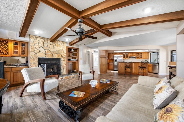 living area with a textured ceiling, wood finished floors, a fireplace, indoor wet bar, and vaulted ceiling with beams