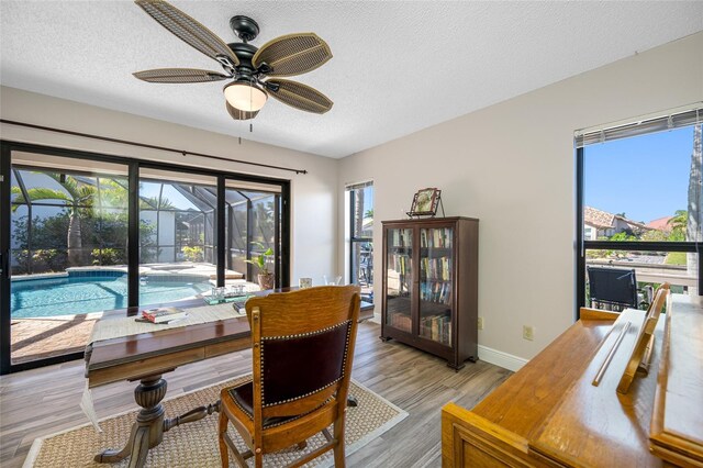 dining room featuring a textured ceiling, light wood-type flooring, baseboards, and a sunroom