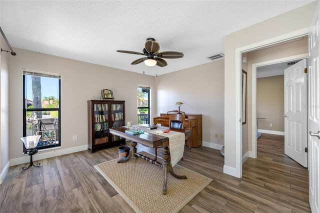 office area with a ceiling fan, baseboards, wood finished floors, visible vents, and a textured ceiling