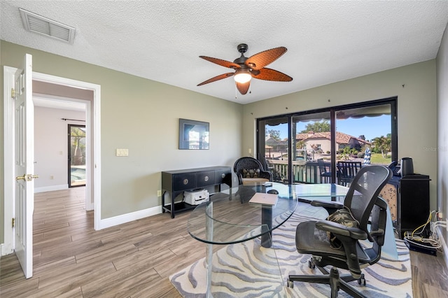 office space featuring visible vents, baseboards, ceiling fan, light wood-style floors, and a textured ceiling