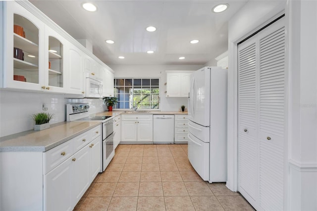 kitchen featuring white appliances, light tile patterned floors, a sink, white cabinets, and glass insert cabinets