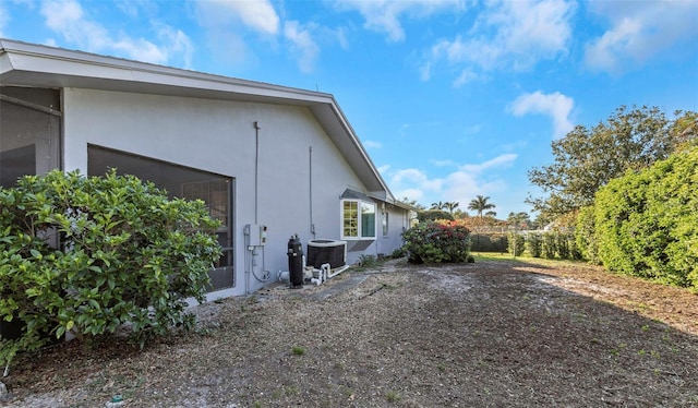 view of side of home featuring fence, central AC, and stucco siding