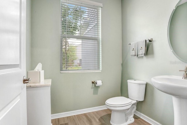 half bath with toilet, baseboards, and wood finished floors