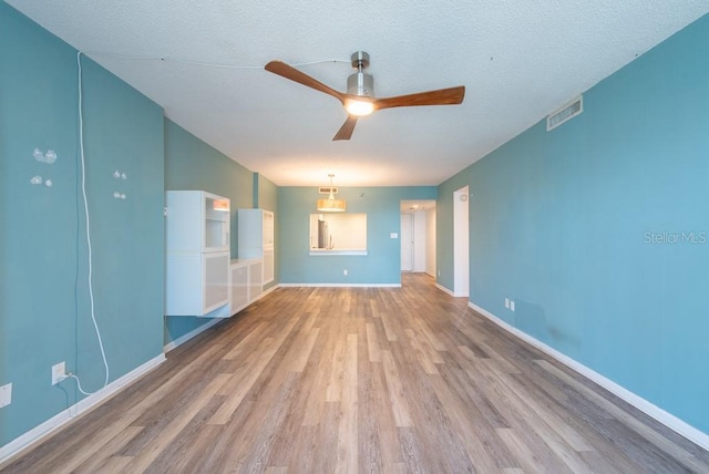 unfurnished living room with visible vents, a textured ceiling, wood finished floors, baseboards, and ceiling fan