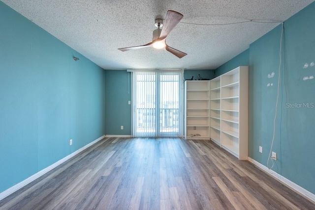 empty room featuring a textured ceiling, wood finished floors, baseboards, and expansive windows