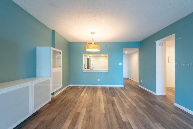 empty room with a textured ceiling, baseboards, and wood finished floors