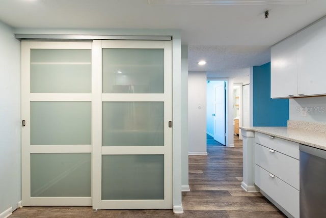 interior space featuring wood finished floors, baseboards, dishwasher, a textured ceiling, and white cabinetry