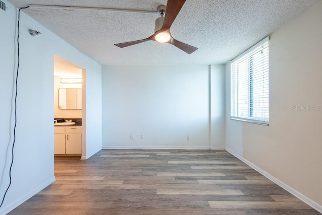 empty room featuring a ceiling fan, visible vents, baseboards, light wood-style flooring, and a textured ceiling