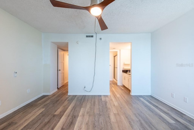 unfurnished bedroom featuring visible vents, light wood-style flooring, a textured ceiling, baseboards, and ceiling fan