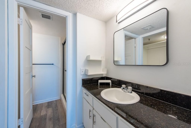 bathroom featuring vanity, wood finished floors, visible vents, a shower stall, and a textured ceiling