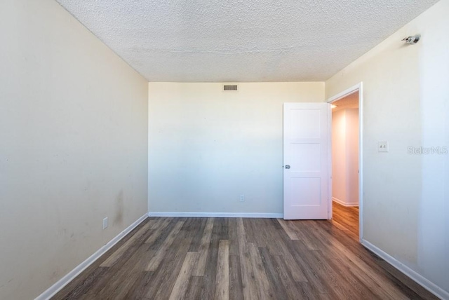 empty room with a textured ceiling, wood finished floors, visible vents, and baseboards