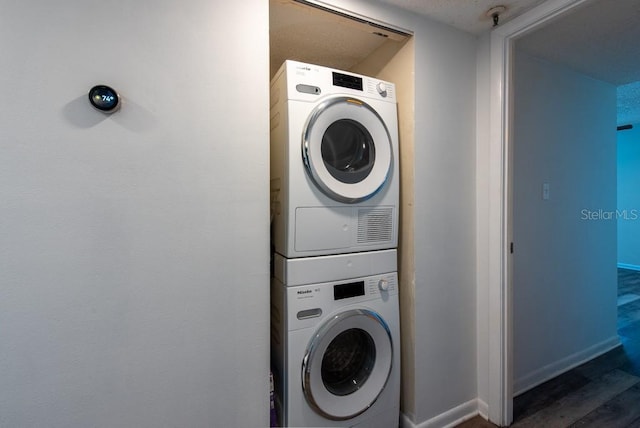 laundry area with laundry area, wood finished floors, baseboards, and stacked washing maching and dryer