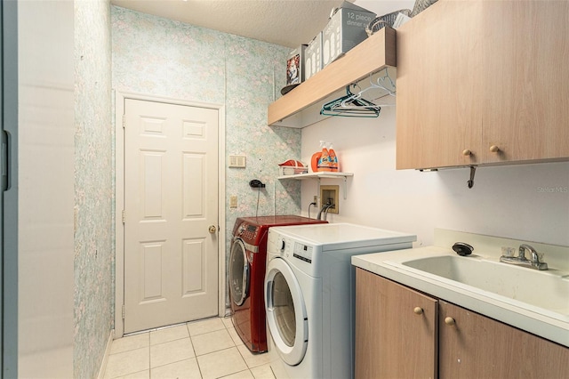 laundry room with a sink, a textured ceiling, cabinet space, light tile patterned flooring, and washing machine and clothes dryer