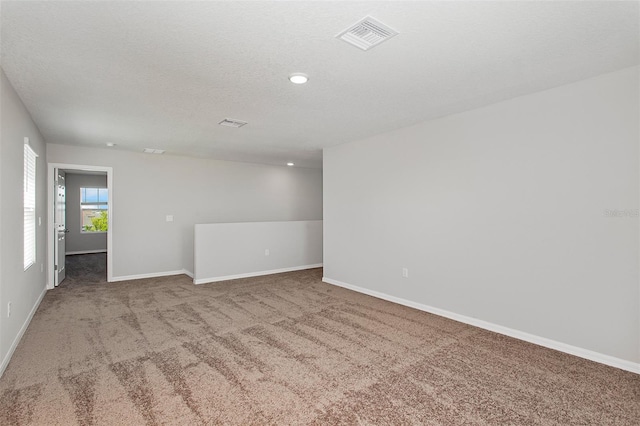 empty room with a textured ceiling, carpet, visible vents, and baseboards