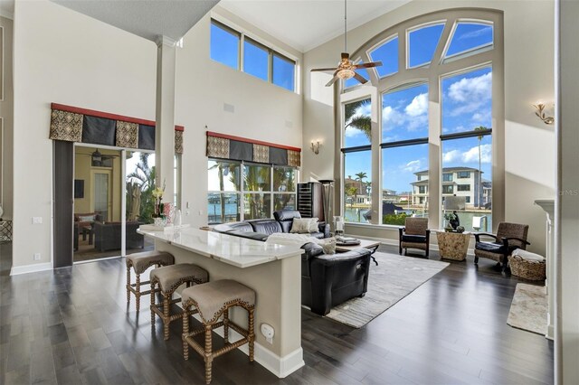 living area featuring decorative columns, baseboards, dark wood-type flooring, and a ceiling fan