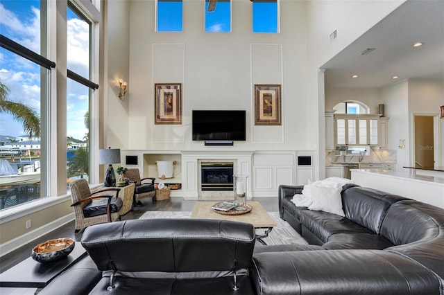 living room with visible vents, baseboards, a fireplace with flush hearth, a high ceiling, and wood finished floors