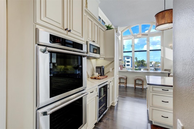 kitchen featuring dark wood-type flooring, beverage cooler, light countertops, appliances with stainless steel finishes, and cream cabinets