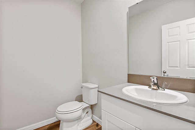 bathroom with baseboards, toilet, wood finished floors, and vanity