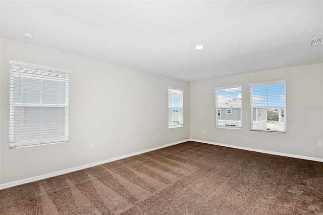 spare room featuring dark carpet, a healthy amount of sunlight, and baseboards