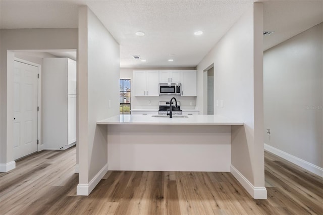 kitchen featuring white cabinets, a peninsula, stainless steel appliances, and a sink