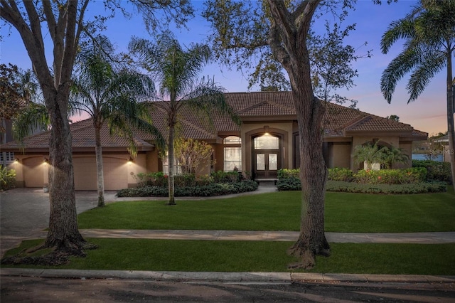 mediterranean / spanish house with a front lawn, a tile roof, stucco siding, driveway, and an attached garage