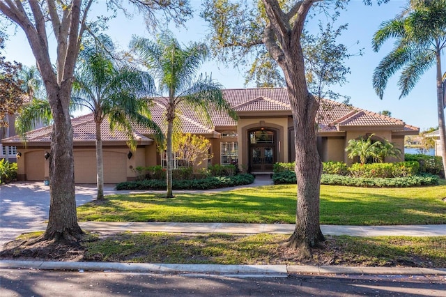 mediterranean / spanish-style house with a tile roof, a front yard, stucco siding, driveway, and an attached garage